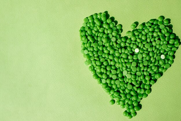 Foto i granuli di cera verdi sono a forma di cuore su uno spazio di sfondo verde per il testo