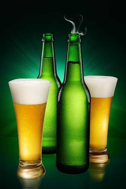 Green wet Bottles and glasses of beer on green background.