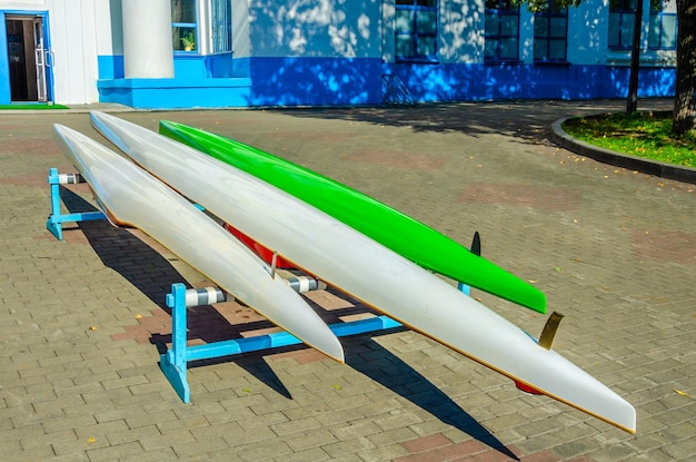 A green and white canoe sits on a blue stand in front of a building.