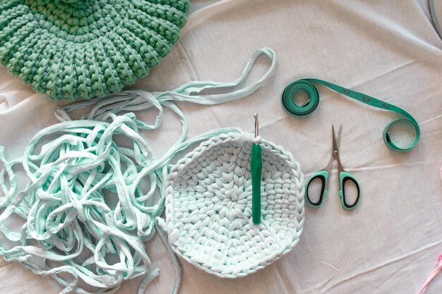 a green and white crochet basket is on a table with scissors and a pair of scissors.