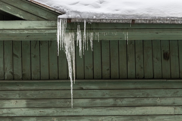 写真 つららがぶら下がっている緑の木造住宅。高品質の写真