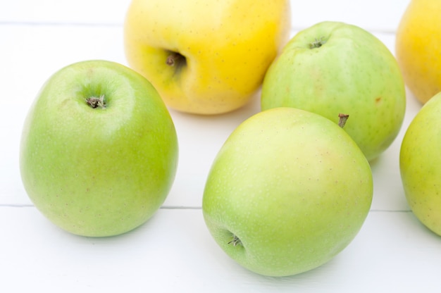 Green and yellow apples on a white wooden background closeup