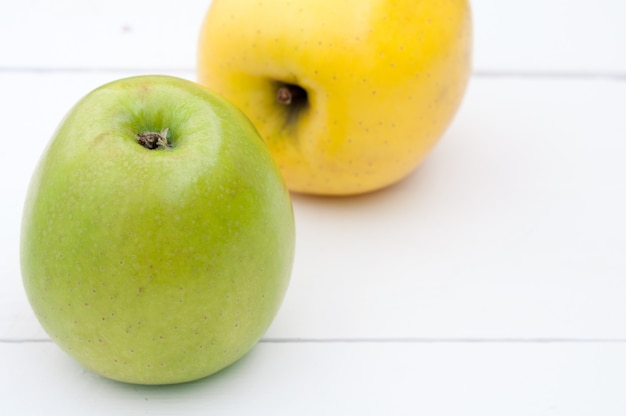 Green and yellow apples on a white wooden background closeup