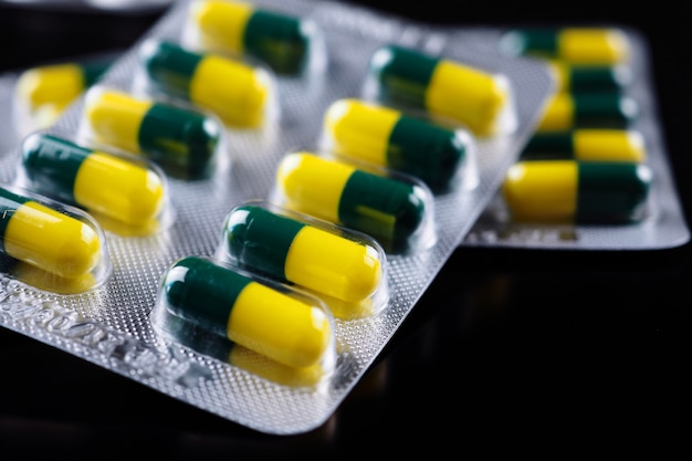 Зеленые желтые таблетки внутри упаковки на черном фоне.