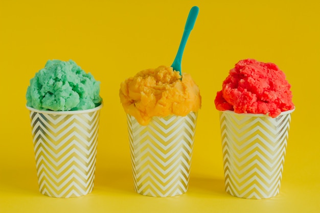 Green, yellow and red fruit ice cream or frozen yogurt in stripped cups   