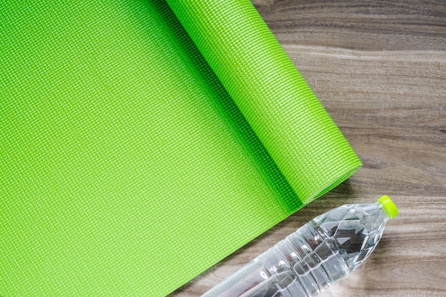 Photo green yoga mat on a wooden background with water bottle