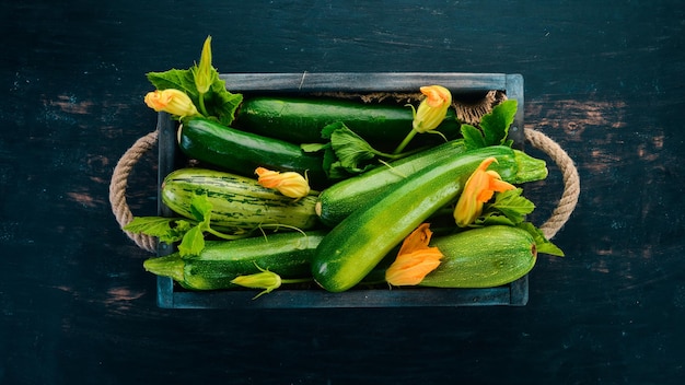 Green zucchini in a wooden box Fresh vegetables On a black wooden background Top view Copy space