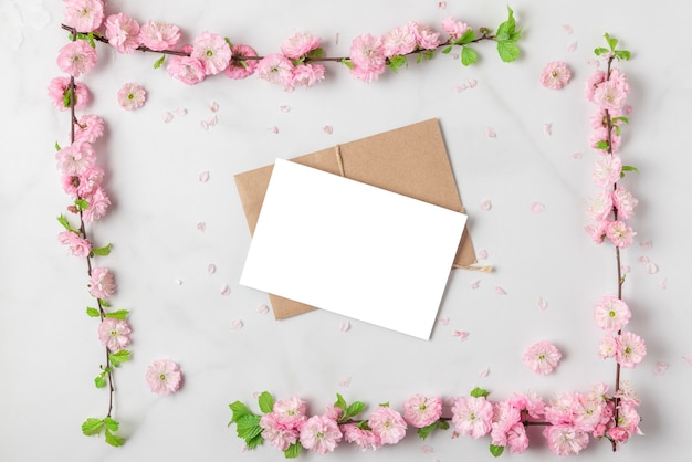 白い大理石の背景に春のピンクの桜の枝で作られたフレームのグリーティングカード。フラットレイ。上面図。コピースペースのある休日や結婚式のレイアウト