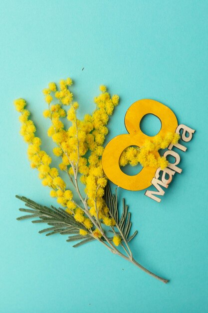 Greeting card for International Women's Day March 8 Blue background with a bouquet of mimosa flowers and the number eight from wood