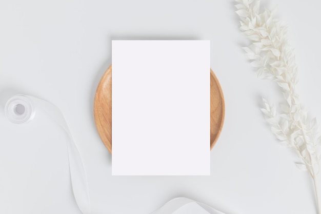 Greeting card or invitation card with white dry flower leaves on wood plate or tray in white background top view