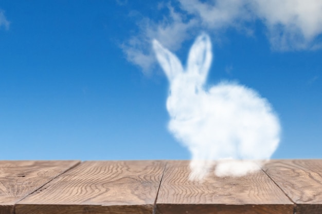 Foto biglietto di auguri con coniglio di pasqua a forma di nuvola su un tavolo di legno contro il cielo nuvoloso con spazio di copia.