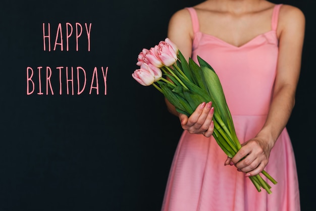 Photo greeting card with the inscription happy birthday. bouquet of pink tulips in the hands