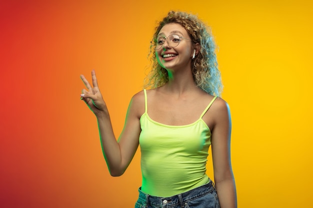 Greeting. Caucasian young woman's portrait isolated on gradient studio background in neon. Beautiful female curly model in casual style. Concept of human emotions, facial expression, youth, sales, ad.