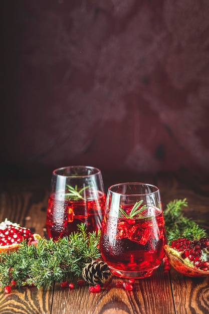 Greeting food Christmas and New Year composition Two glasses of pomegranate drink surrounded pine branches claret bordeaux concrete background Close up shallow depth of the field