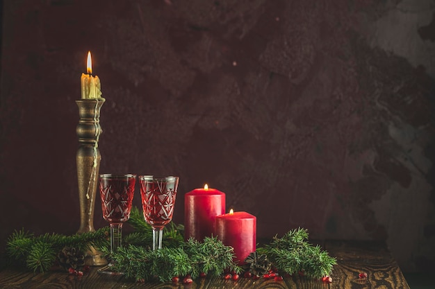 Greeting food Christmas and New Year composition Vintage glass of pomegranate drink surrounded pine branches and festive candles dark background Close up shallow depth of the field