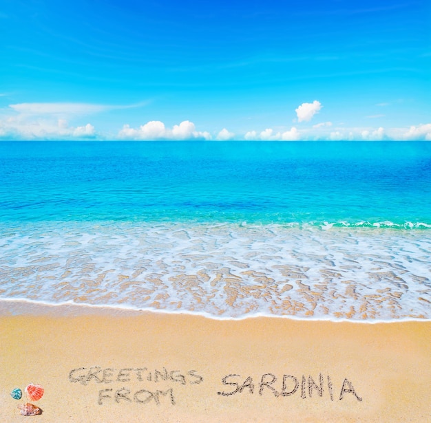 Saluti dalla sardegna scritti su una spiaggia tropicale