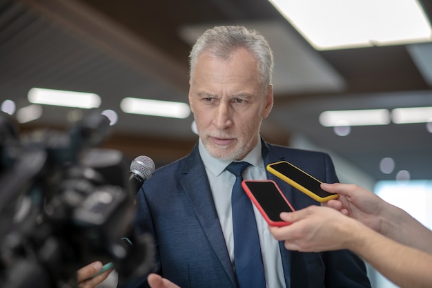 Grey-haired bearded man looking serious while having the press conference