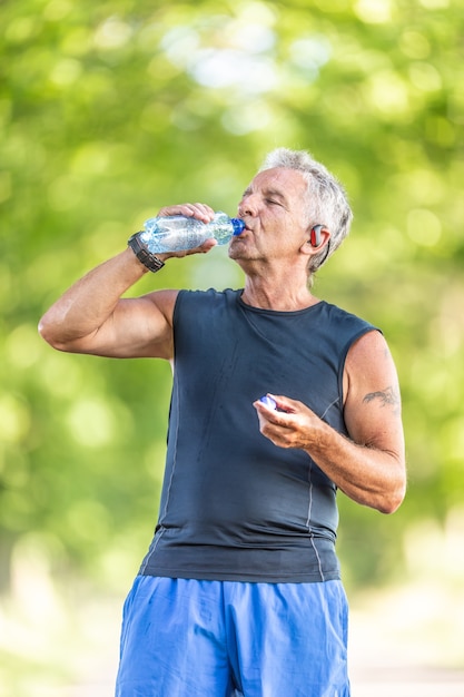 70代の白髪の男性は、自然の中で運動した後も健康で水を飲みます。