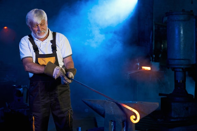 Grey haired man processing molten metal on anvil