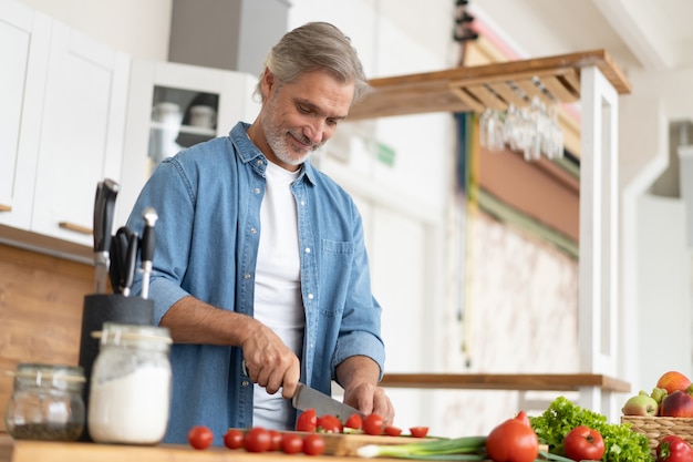 grey-haired mature handsome man preparing delicious and healthy food in the home kitchen.