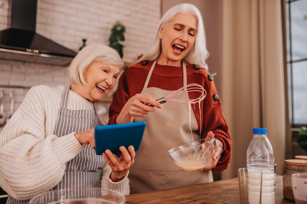 Grey-haired smiling lady in apron showing something on her smartphone