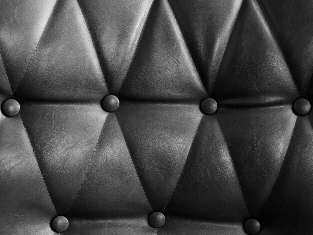 Grey jeather sofa with pins and buttons texture background. Close up of vintage black leather sofa surface.