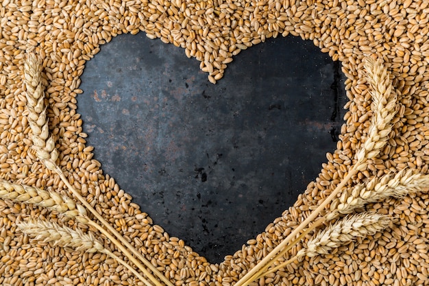 Photo grey metal heart from seeds of ripe golden wheat