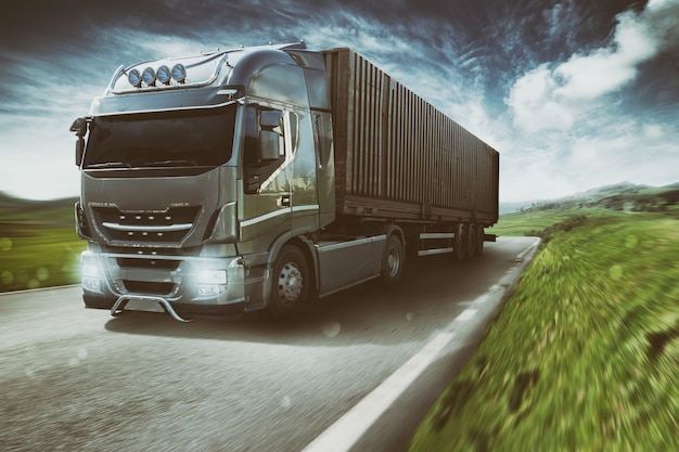 Grey truck moving fast on the road in a natural landscape with cloudy sky