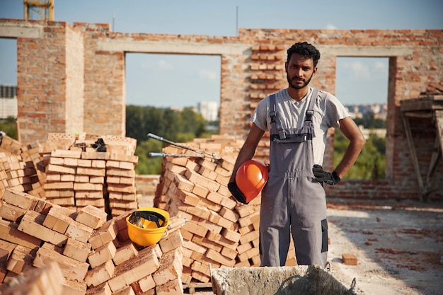Photo in grey uniform handsome indian man is on the construction site