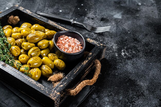 Grieks Gegrilde olijven met knoflook, olijfolie en kruiden in houten dienblad. Zwarte achtergrond. Bovenaanzicht. Ruimte kopiëren.