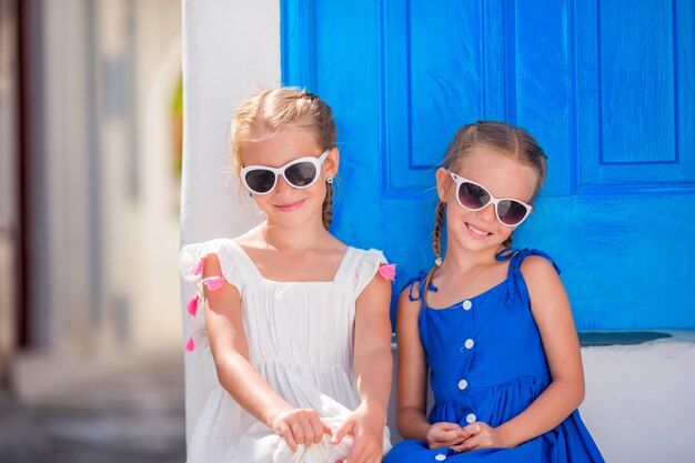 Grieks portret van kleine glimlachende meisjes die dichtbij oude blauwe deur in grieks mykonos-dorp zitten