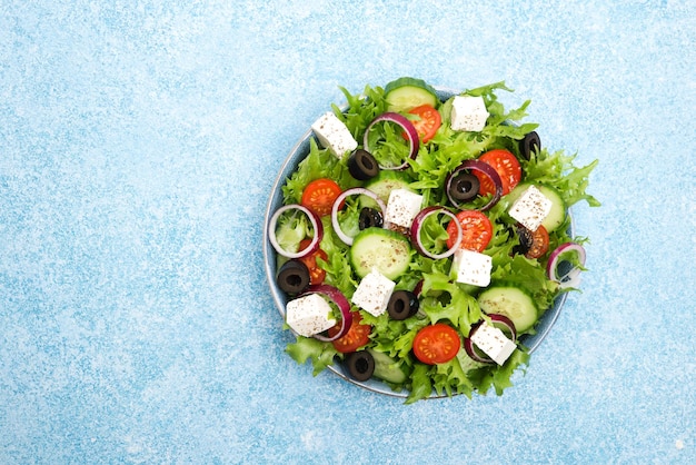 Griekse salade met tomaten, komkommers, olijven en fetakaas in een bord op een betonnen ondergrond, bovenaanzicht, kopieerruimte