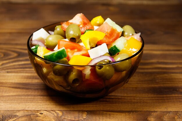 Griekse salade met verse groenten, fetakaas en groene olijven in glazen kom op houten tafel