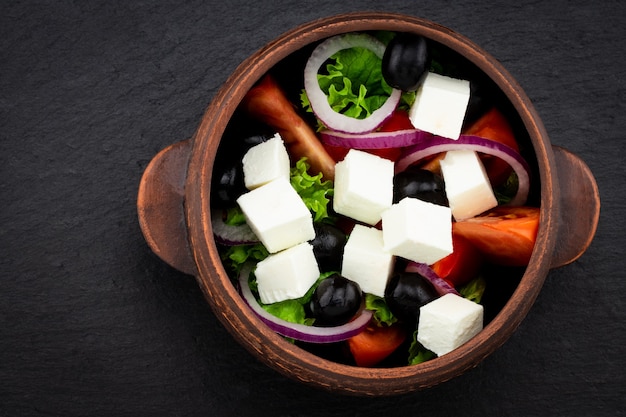 Griekse salade met verse groenten, fetakaas en zwarte olijven op een donkere achtergrond.