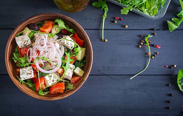 Griekse salade met verse tomaat, komkommer, rode ui, basilicum, fetakaas, zwarte olijven en Italiaanse kruiden. Bovenaanzicht