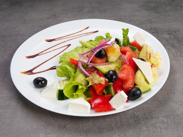 Griekse salade op een witte plaat op een grijze achtergrondconceptvegetarisme