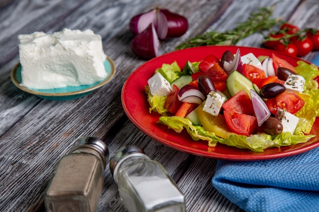 Griekse salade van verse komkommer, tomaat, paprika, sla, rode ui, fetakaas en olijven met olijfolie op houten achtergrond. Gezond eten