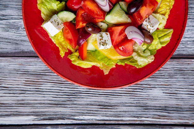 Griekse salade van verse komkommer, tomaat, paprika, sla, rode ui, fetakaas en olijven met olijfolie op houten ondergrond. Gezond eten, bovenaanzicht