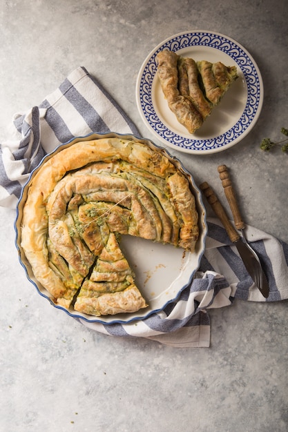 Griekse taart spanakopita over concrete achtergrond. Ideeën en recepten voor vegetarische of veganistische spinazietaart van fillogebak in plakjes gesneden