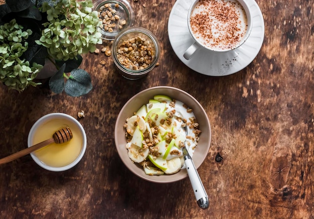 Griekse yoghurt met granola-banaanappel en cappuccino op een houten bovenaanzicht als achtergrond Heerlijk ontbijt