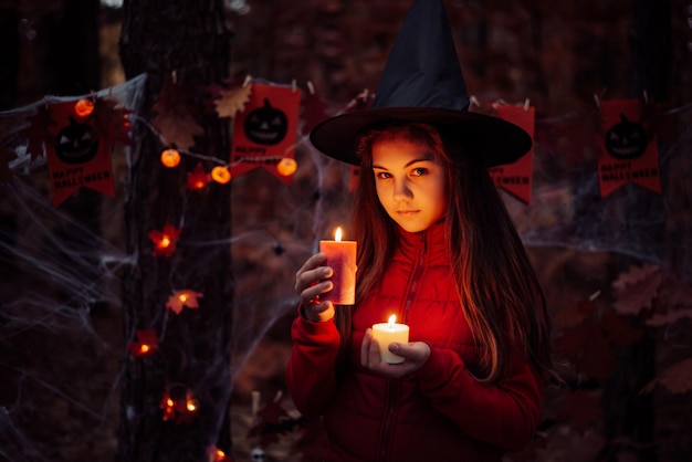 Griezelige foto van een klein schoolmeisje met rode en witte kaars laat in het herfstbos halloween-vieringsconcept van hekserij in het bos