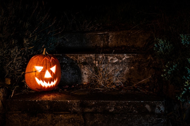 Griezelige halloween-pompoenlantaarn op betonnen trappen in de tuin 's nachts