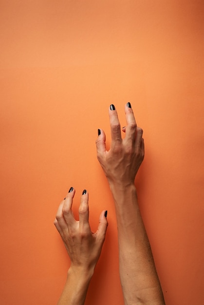 Griezelige vrouw Halloween handen met zwarte nagels op oranje achtergrond