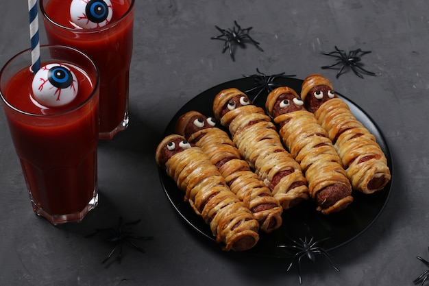 Griezelige worstmummies en tomatensap voor Halloween-feest op zwarte plaat.