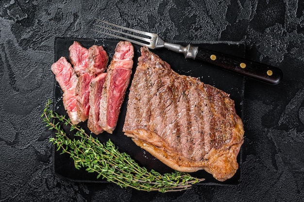 Griiled on BBQ sliced Striploin marbled beef meat steak Black background Top view