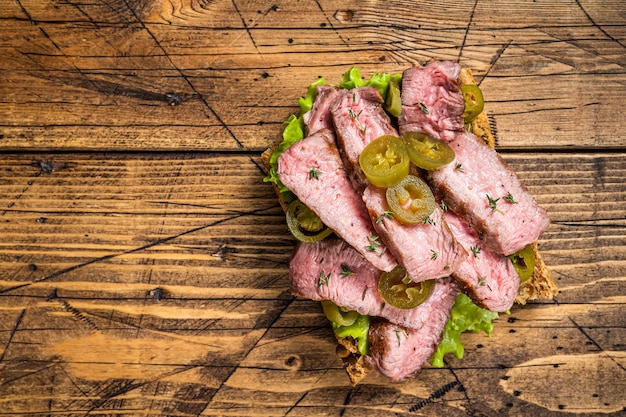 Griiled Steak sandwich with sliced beef, rocket and vegetables on bread. Wooden background. Top view. Copy space.