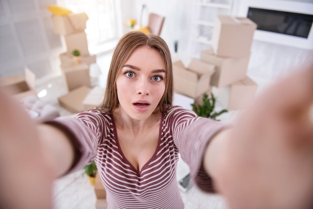 Foto grijp het moment. charmante jonge vrouw die een selfie neemt in haar nieuwe appartement terwijl ze voor de camera poseert en deze met twee handen vasthoudt