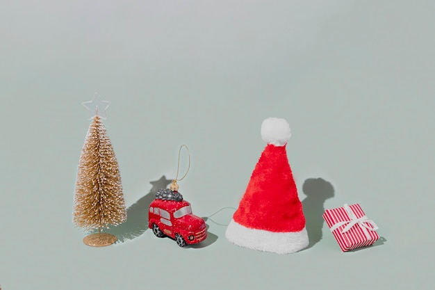 Grijze achtergrond met kerstmis of nieuwjaar symbool attribuut objecten en symbolische items concept. roze geschenkdoos aanwezig met lint, klein rood taxi-autospeelgoed, dennenboom en rode feestelijke santa hap of pet