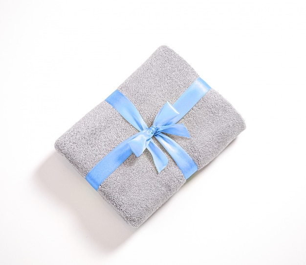 Grijze badstofhanddoek die tegen witte achtergrond wordt gevouwen, handdoek die door blauw geïsoleerd lint wordt gestapeld en wordt gebonden