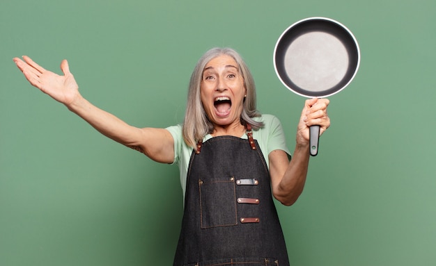 Grijze haar mooie middelbare leeftijd chef-kok vrouw met een pan